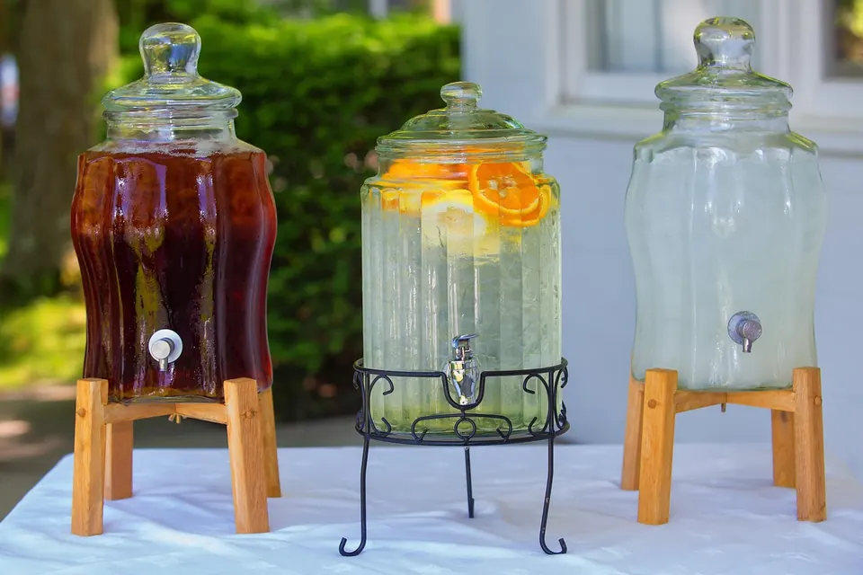 Trois distributeurs de boissons en verre avec thé glacé, eau citronnée et limonade sur une table extérieure