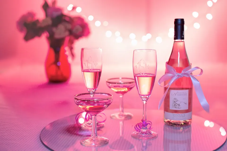 Coupes et flûtes de vin rosé avec une bouteille nouée d’un ruban sur une table rose