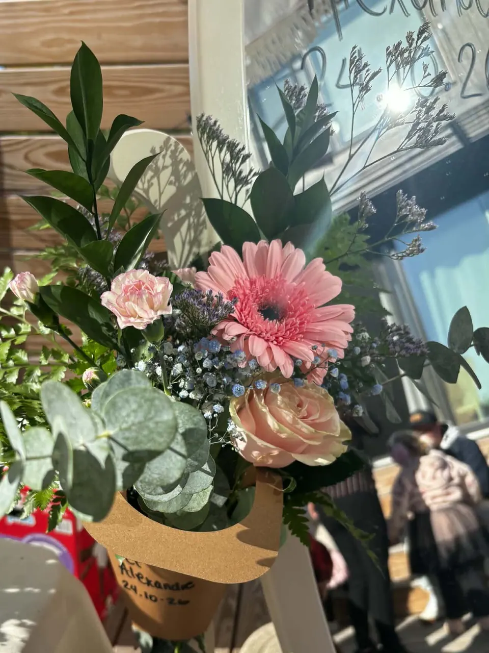 Bouquet composé par une invitée : gerbera rose, rose pêche, œillet, gypsophile bleu et eucalyptus dans un cornet kraft