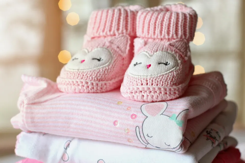 Chaussons de bébé roses tricotés posés sur une pile de vêtements de bébé pliés