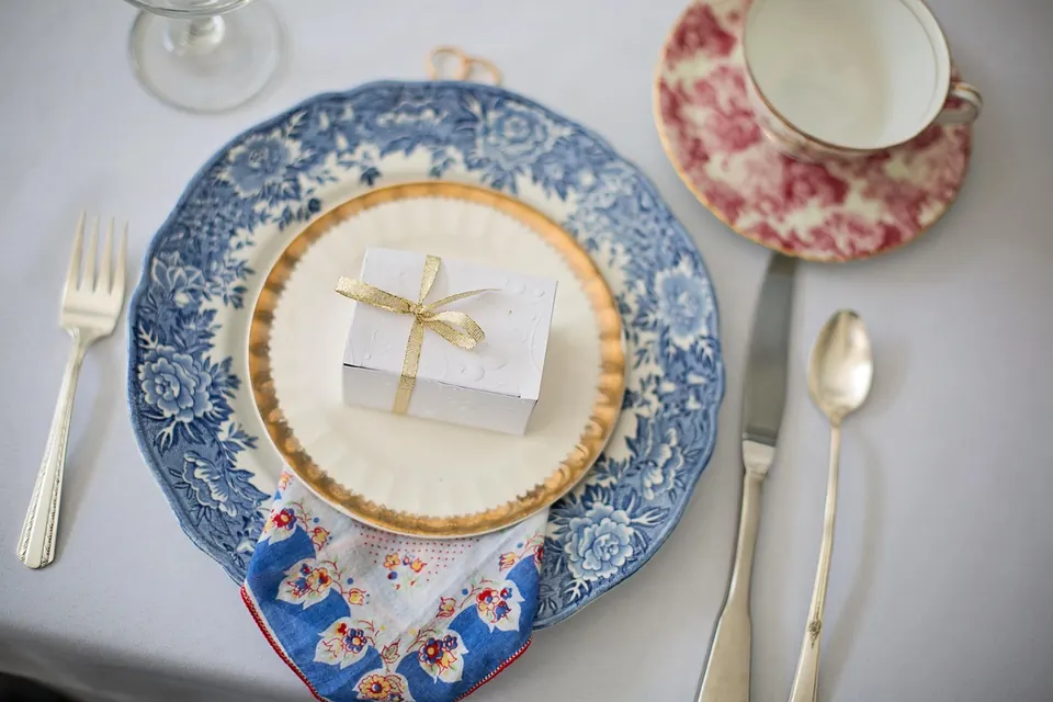 Couvert de vaisselle ancienne bleue et rose avec une petite boîte cadeau blanche nouée d’un ruban doré
