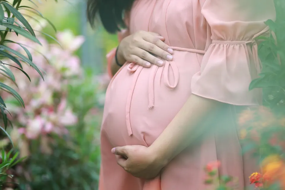 Future maman en robe rose qui tient son ventre, entourée de fleurs