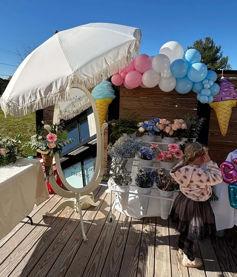 Installation complète du bar à fleurs avec parasol, miroir, arche de ballons et une fillette qui choisit ses fleurs