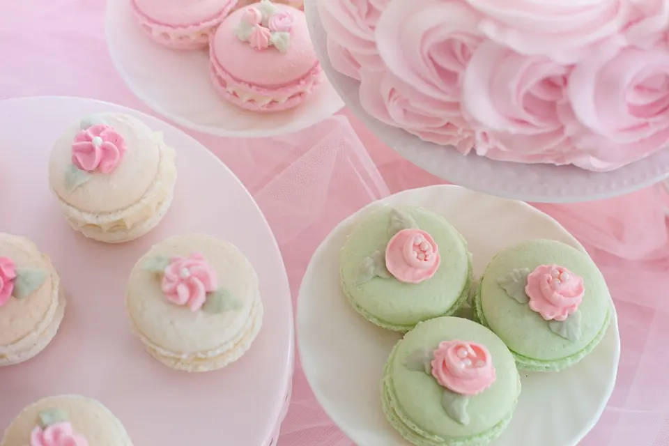 Macarons verts et crème décorés de roses en glaçage sur des assiettes blanches