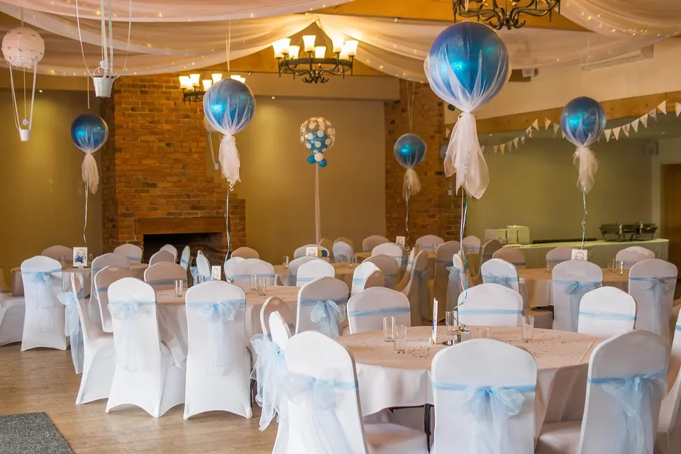 Salle de réception décorée pour un shower de bébé avec ballons bleus transparents et housses de chaises blanches