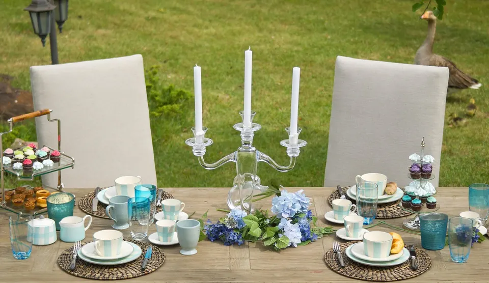 Table dressée dans un jardin avec chandelier, tasses à thé turquoise, hortensias bleus et présentoir de petits gâteaux